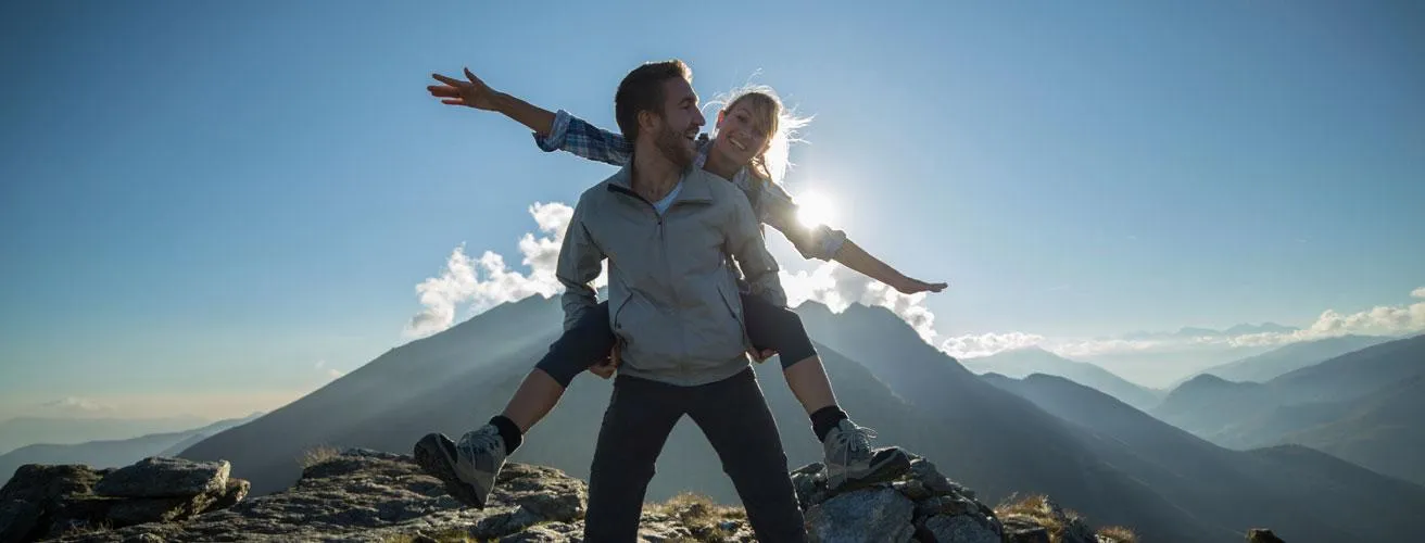 Man piggybacking a woman on a mountain trail